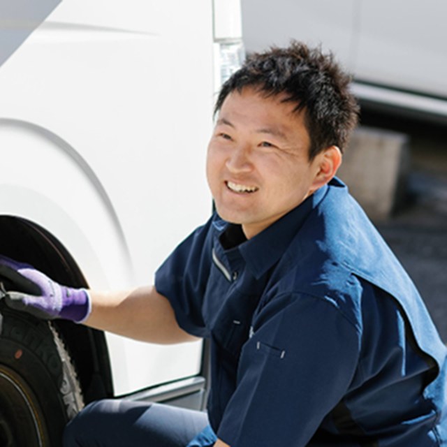 代表の馬場保孝。作業着姿で車両のそばに立ち、笑顔でこちらを見ている